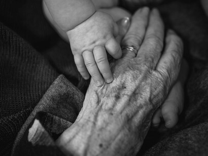 Two hands, one just beginning and one full of memory, touch the mystery of being