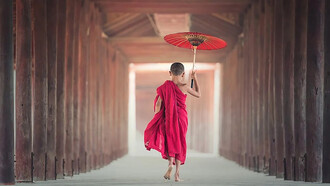 A young monk boy walking with an umbrealla