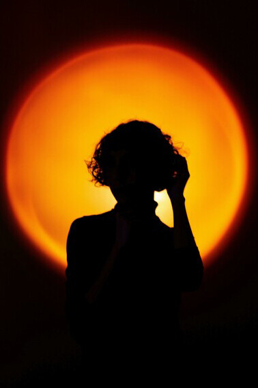 A lone figure silhouetted against a reddish-yellow illuminated window in a dark room
