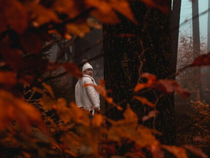 A woman walks through a foggy forest covered in red autumn leaves