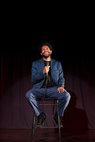 A man performing stand-up comedy on stage in a lively comedy club atmosphere