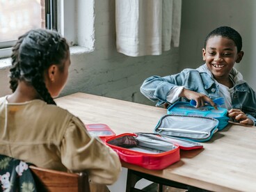 Smiling Black schoolboy interacting with a girl during lunch, with a bright and colorful lunchbox