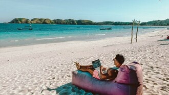 A man sitting on a bean bag on the beach, working on his laptop in Lombok