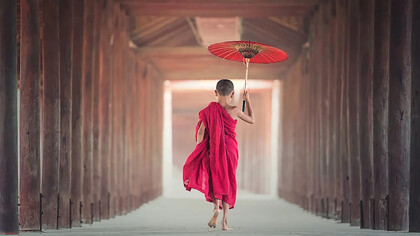 A young monk boy walking with an umbrealla