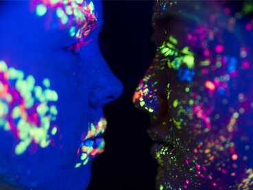 Two faces illuminated by neon paint, reflecting the how energies communicate beyond words