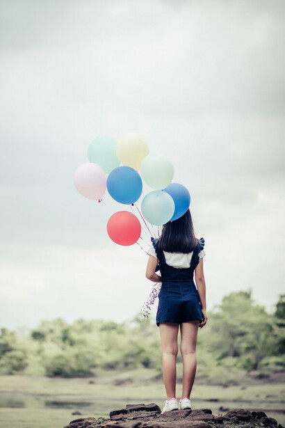 A young woman holding vibrant balloons in the natural landscape, celebrating the simple pleasures of life, self-care, and the calming embrace of sunlight on her skin