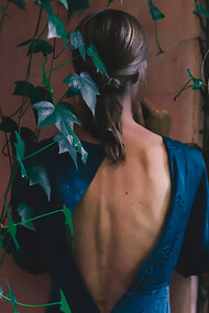 A woman in a blue dress, viewed from behind, standing near an old building