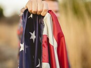 A person holds a tightly folded American flag in their hand, symbolizing national identity and the complex questions surrounding what truly makes a nation great