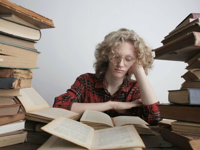 Rapaz lê cercado por muitos livros. Mudando somente um hábito em sua vida você muda o seu destino, dentre os hábitos a serem considerados para a mudança um dos mais importantes é desenvolver o hábito da leitura, bons livros fazem mudanças internas em você que nada mais faz. Portanto, quem acredita que os livros são chatos e é um saco ler, tende a ficar amarrado no ponto em que está atualmente, tendo dificuldade na progressão de sua vida