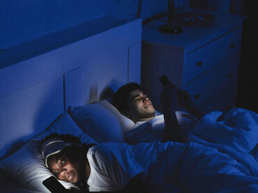 A couple lying in bed, using their phones with the lights turned off