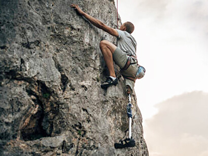 A man with a disability rock climbs using a prosthetic leg, demonstrating strength and determination