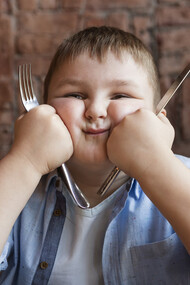 An obese boy holding cutlery, ready to eat