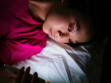 People resting on a bed, distracted by their smartphone