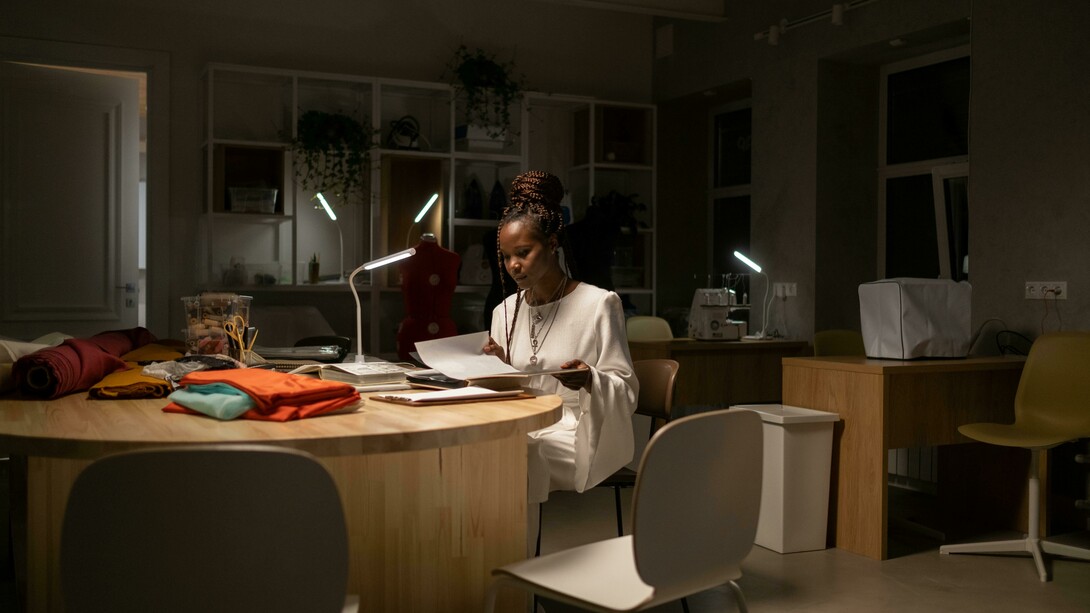 A young African American fashion designer working late in her sewing workspace, a creative professional deep in thought