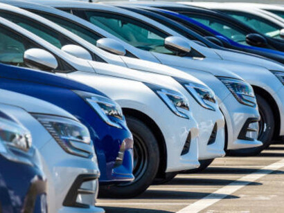 A row of newly manufactured cars awaits export in a large parking lot