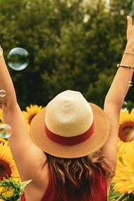 Una donna gioiosa di schiena in un campo di girasoli. La gioia è un'emozione universale, un inno di felicità che risuona attraverso l'anima umana in una sinfonia di colori e sensazioni