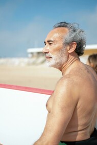 Idoso se prepara para surfar no mar. Lidar com as mudanças não é fácil. No entanto, ao equilibrar os sentimentos de perdas com fatores positivos, o idoso pode permanecer saudável e continuar a se reinventar ao passar pelas idades marcantes de 60, 70, 80 anos e além