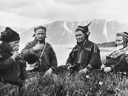 A group of Mountain Sami people in Lyngen, Troms in Norway. This photo postcard was published by T. Høegh in 1928. According to P.L. Smiths book "Kautokeino og Kautokeino-lappene", from 1938, the photo shows "Sommerliv på Uløen" ("Summer life on Uløya") and the photographer was A. Giæver