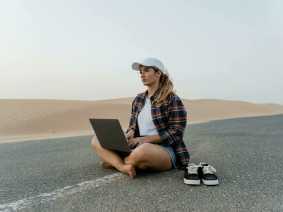 A traveler in a black shirt works remotely on her laptop beside a quiet desert road, embodying the spirit of digital nomadism