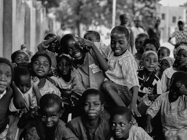 In this black-and-white image, a group of war-torn people, especially children, appear hungry and filled with sadness