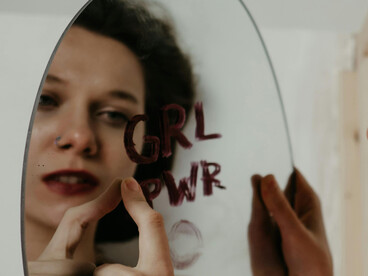A girl stares at her reflection on a scribbled mirror