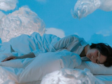 A sleeping woman surrounded by small weightless clouds, reflecting how sleep cycles help the body and mind reset