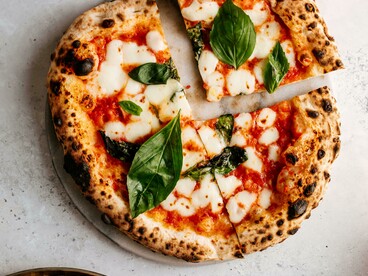 Hands present a pizza, poised for the sacred first bite