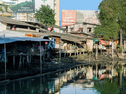 Slums on the riverbank face the distant city skyline, symbolizing inequality and the gap between rich and poor