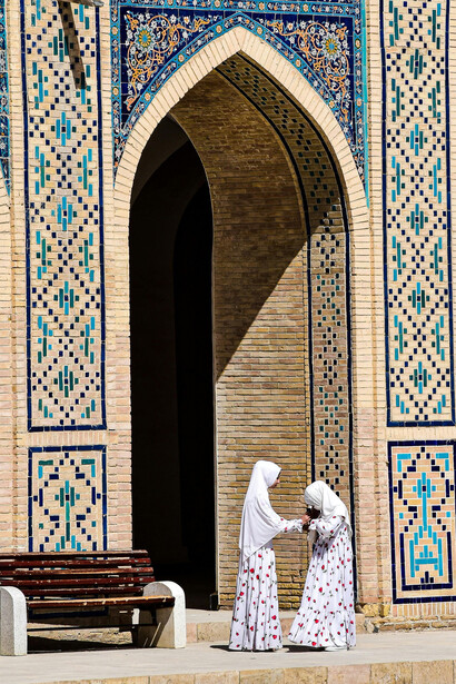 Women at the beautifully decorated entrance of a mosque in Bukhara, Uzbekistan, highlighting the elegance of Islamic architecture and Uzbek tradition