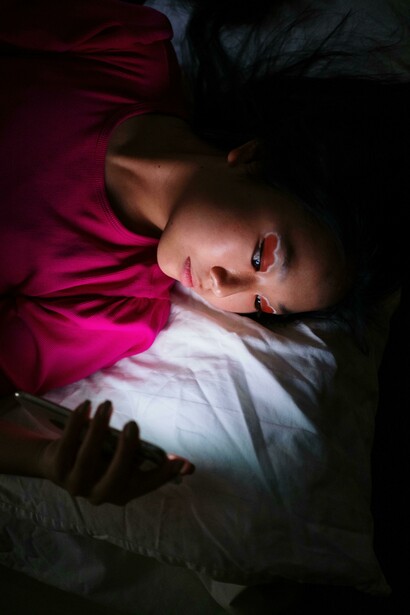 People resting on a bed, distracted by their smartphone