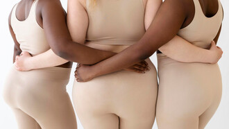 Three women stand together, arms intertwined, their bodies visible rejecting narrow ideals 