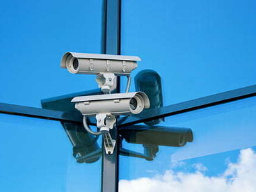 A CCTV camera mounted against a clear blue sky, symbolizing facial recognition technology