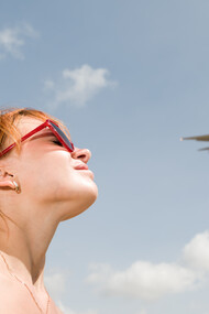 Young woman watching an airplane in the sky, feeling a sense of longing