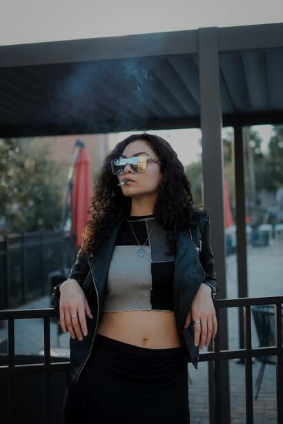 Outdoors, a fashionable woman in sunglasses is smoking
