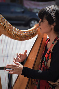 A beautiful Japanese woman in a black long-sleeve shirt playing the harp on a street in Kyoto, Japan