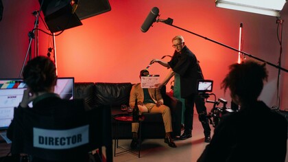 A director in a black shirt holds a clapperboard during filming