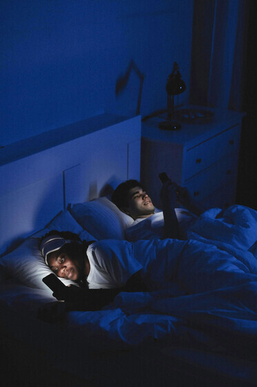A couple lying in bed, using their phones with the lights turned off