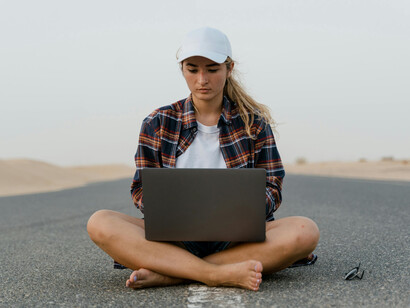 A woman sits on a roadside beside the desert, working remotely on her laptop — a modern traveler embracing the nomadic life