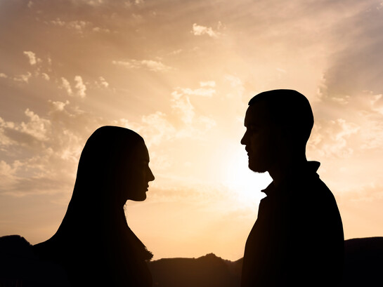 Silhouette di un uomo e una donna che si guardano, con un cielo al tramonto dai colori caldi sullo sfondo