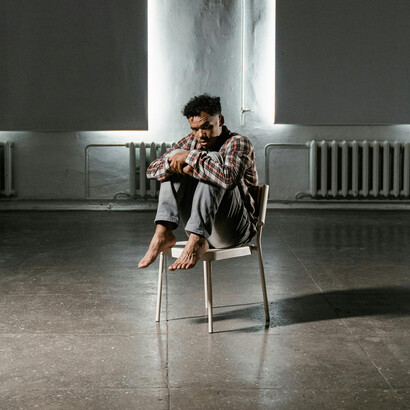 Seated alone on a chair, a man reflects in stillness—his posture echoing a journey of existential longing and inward transformation