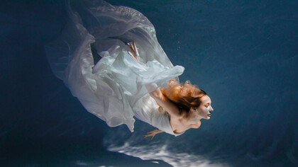 A graceful body suspended in water in a flowy white dress, conveying a weightless, unhurried state that mirrors emotional release