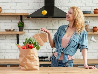 A woman prepares food in the kitchen, with a variety of vegetables spread around her