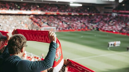 A fan holding a Liverpool scarf high in the stands