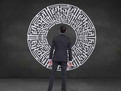 Uomo di schiena in abito scuro davanti a un grande labirinto circolare: "Il futuro ti appare nebbioso o spento perché la corteccia prefrontale e la tua modalità di funzionamento sono al risparmio: non è un problema psicologico, è un problema energetico"