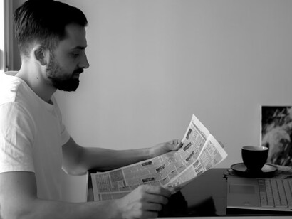 A man sitting at a desk reading a newspaper, reflecting on the role of AI in journalism and the evolving relationship between technology and truth