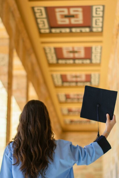 A brunette woman holds her graduation cap gently in hand, capturing a quiet moment of reflection between achievement and uncertainty