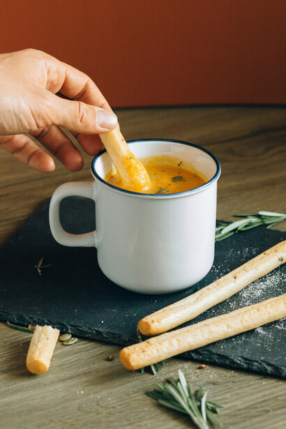 A white ceramic mug brimming with hot winter soup, finished with a sprinkle of fresh green leaves
