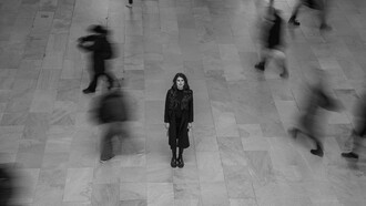 A solitary woman standing alone in a busy New York terminal, capturing the contrast between personal loneliness and the surrounding crowd, USA