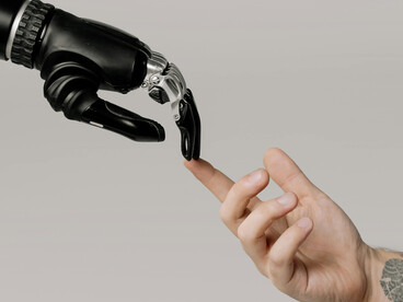 A human and robotic hand meet, representing the intersection of technology and humanity
