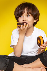 A cute boy enjoying donuts surrounded by flowers on a vibrant yellow desk